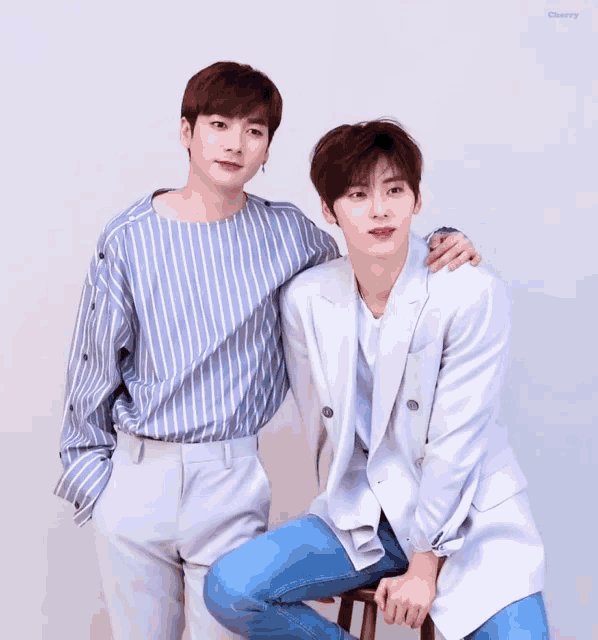 two young men standing next to each other with one wearing a striped shirt and the other sitting on a stool