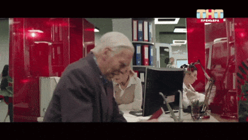an older man sits at a desk in front of a computer screen with the letters tht on it