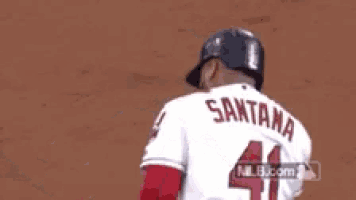 a baseball player wearing a white jersey with the name santana on it is standing on a field .
