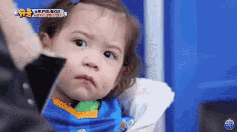 a little girl wearing a blue and orange shirt is making a funny face