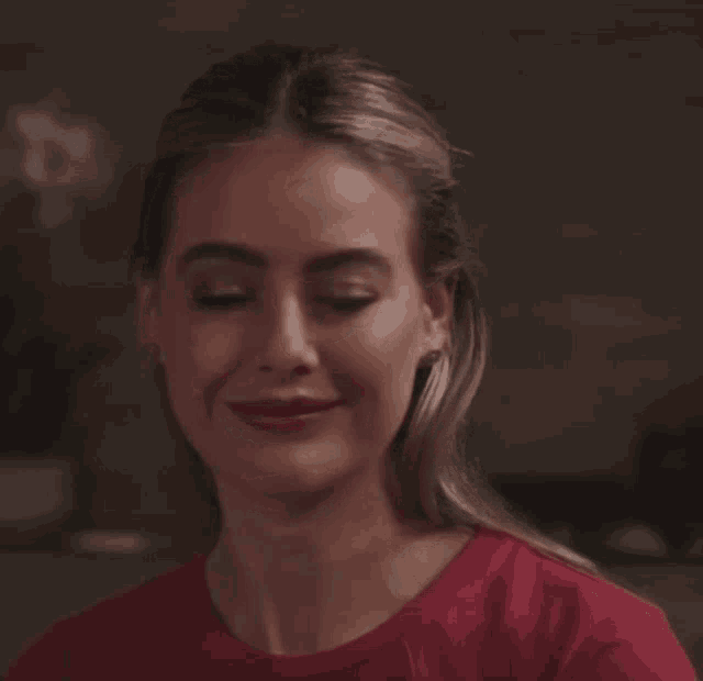 a woman in a red t-shirt is smiling with her eyes closed