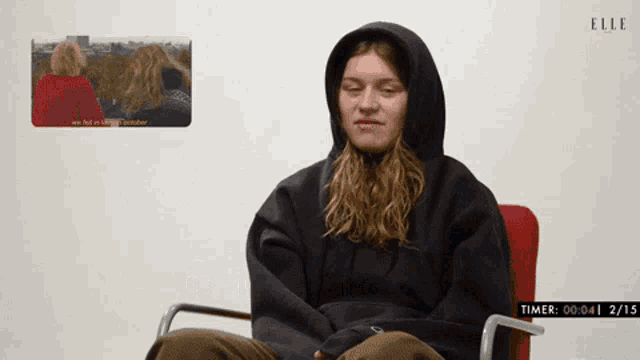 a woman wearing a black hoodie is sitting in a chair with a timer on the bottom right