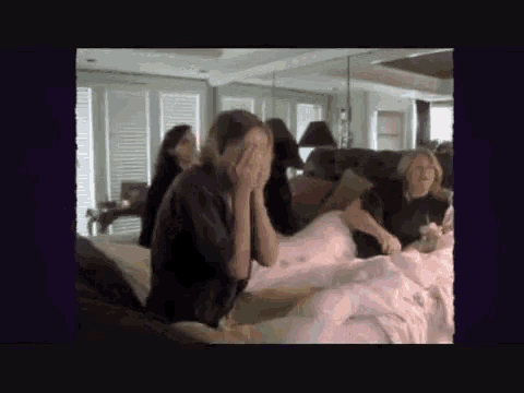 a group of people are sitting on a bed and one woman is covering her face