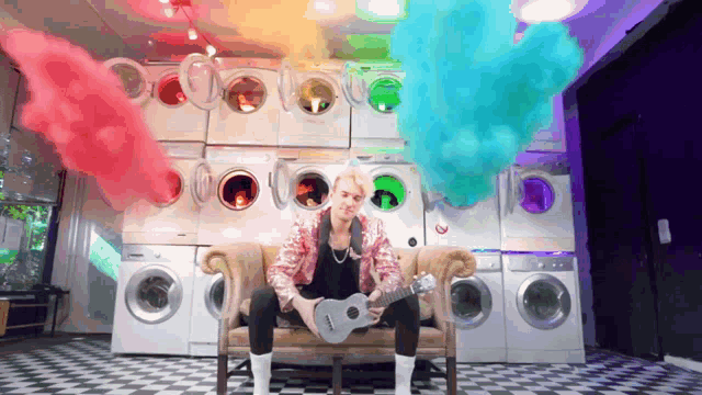a man is sitting on a couch playing a guitar in front of a wall of washing machines