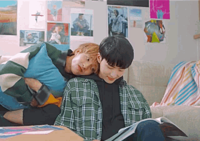two young men are sitting on a couch with a book and a pillow .