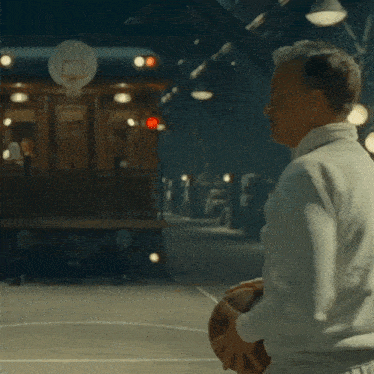 a man in a white jacket is standing in front of a train and a basketball hoop