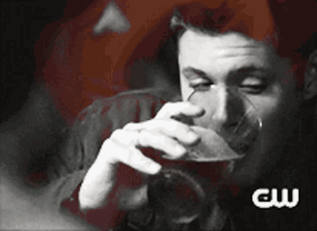 a man drinking from a glass with the cw logo on the bottom