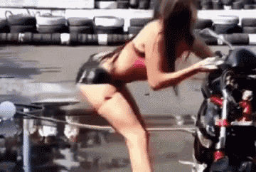 a woman in a bikini is kneeling on a motorcycle .