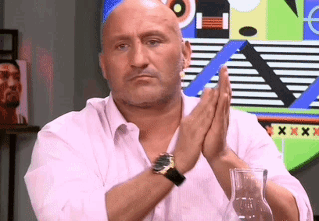 a bald man in a pink shirt with a watch on his wrist is clapping his hands