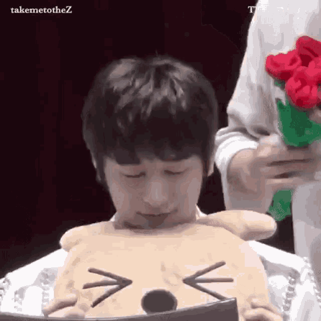 a young boy is holding a stuffed animal in front of his face while another person holds a bouquet of flowers .