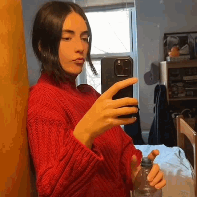 a woman in a red sweater is taking a picture of herself in the mirror .