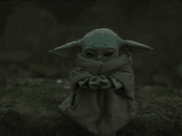 a baby yoda doll is sitting on a rock in the grass