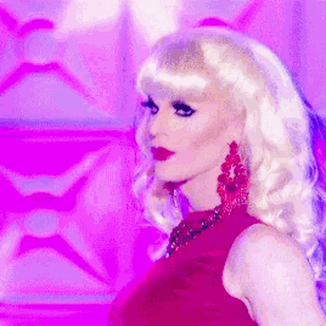a drag queen wearing a red dress and earrings is standing in front of a purple background .