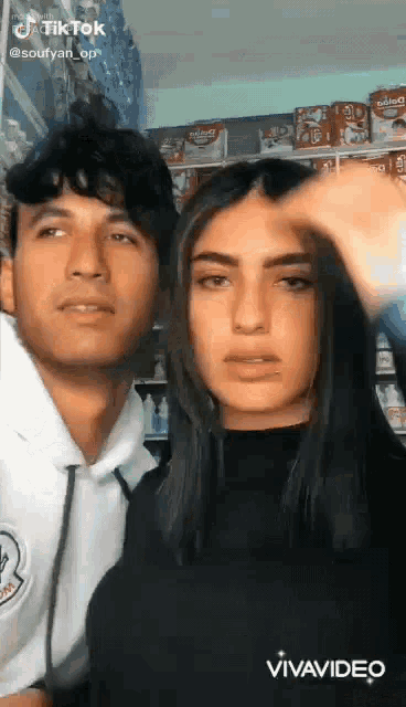 a man and a woman are standing next to each other in a store . the man is touching the woman 's hair .