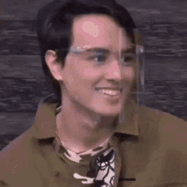 a man wearing glasses and a face shield is smiling and looking at the camera .