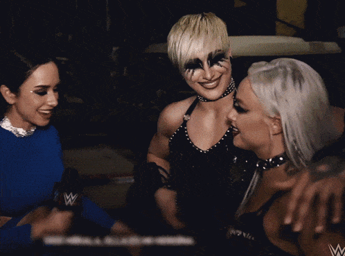 three women are standing next to each other and one of them has a microphone with the letter w on it