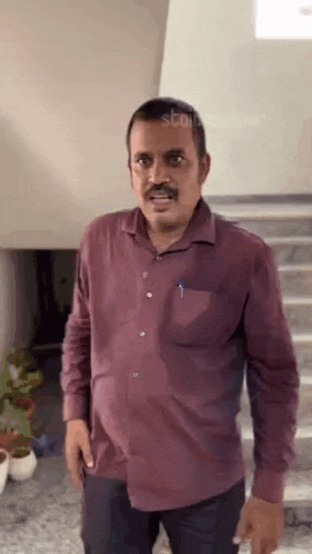 a man in a maroon shirt is standing in front of stairs .