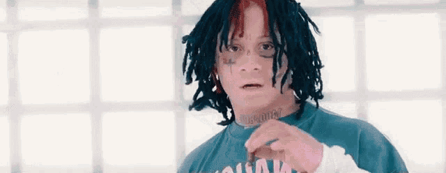 a man with dreadlocks and a tattoo on his face is wearing a blue shirt and holding a cigarette .