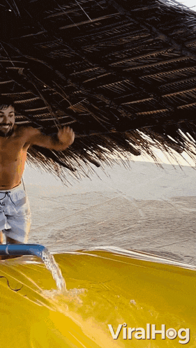 a shirtless man is standing under a thatched roof while water is pouring out of a hose