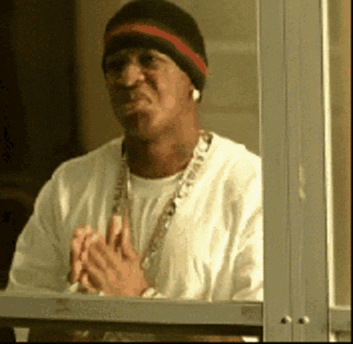 a man wearing a beanie and a necklace looks out of a window