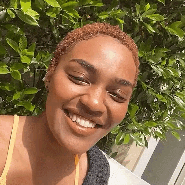 a woman with short hair is smiling in front of a bush