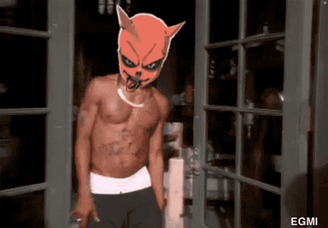 a shirtless man with a devil mask on stands in front of a door