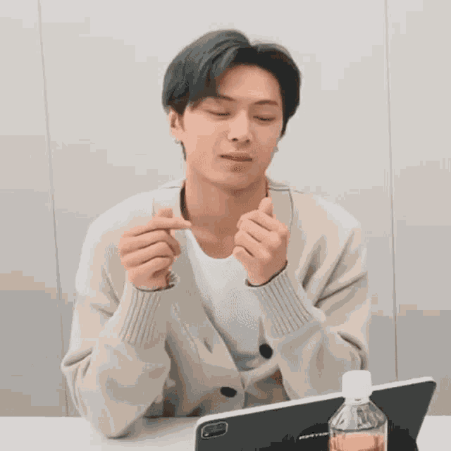 a man is sitting at a table with his eyes closed and making a heart shape with his hands .