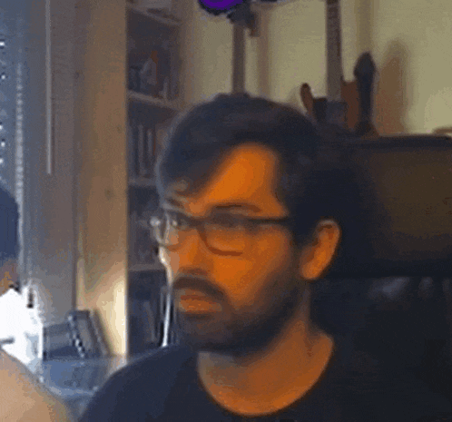 a man with a beard and glasses is sitting in front of a guitar .