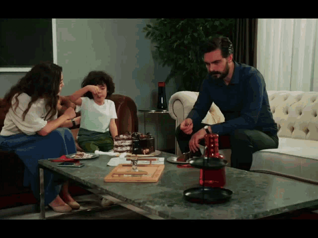 a man and a woman sit on a couch while a little boy sits at a table with a cake on it