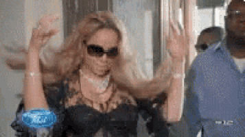 a woman wearing sunglasses and a black dress is dancing in front of a man .