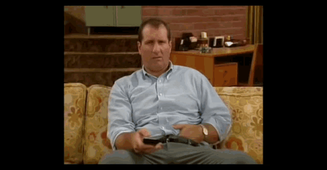 a man in a blue shirt sits on a couch holding a remote control