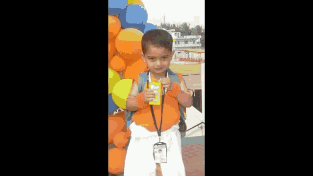 a young boy is standing in front of balloons holding a juice box