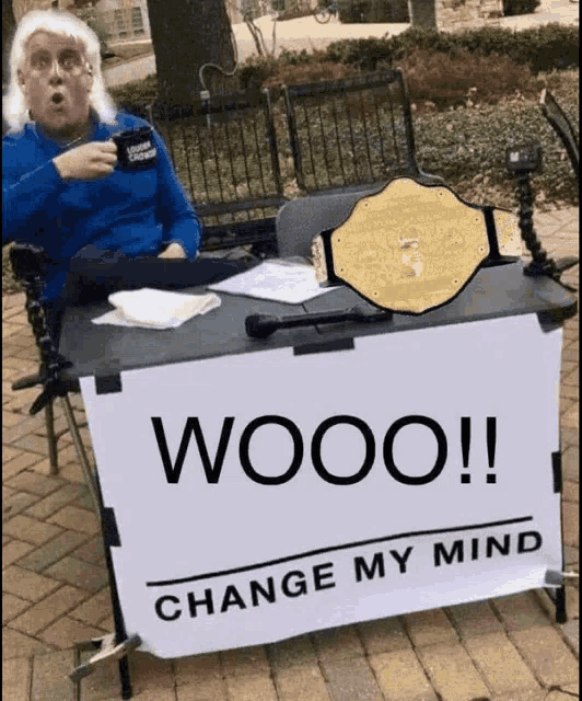 a man is sitting at a table with a sign that says wooo change my mind