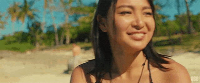 a woman in a bikini is smiling and looking at the camera on a beach .
