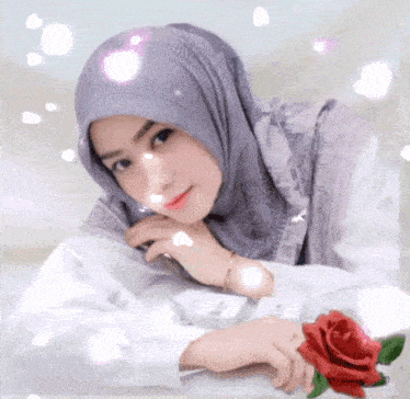 a woman in a hijab is sitting at a table with a red rose in front of her .
