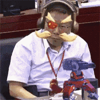 a man wearing a mask and headphones is sitting at a desk with a toy robot in front of him .