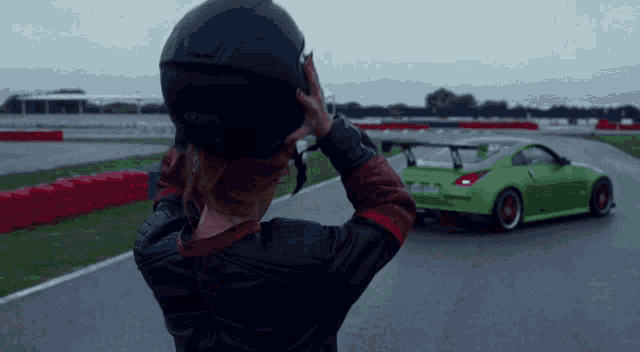 a woman wearing a helmet looks at a green sports car on a race track