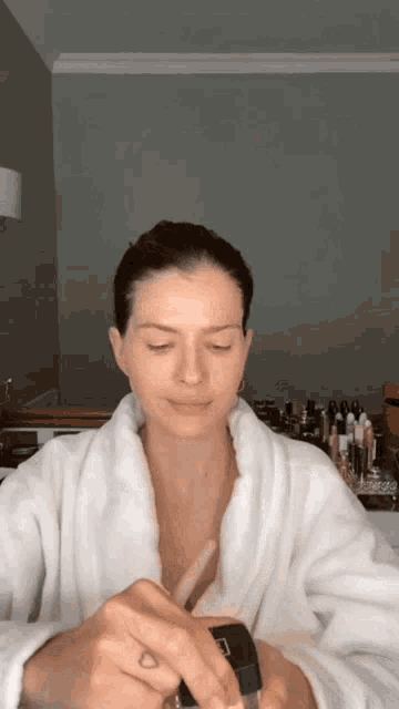 a woman in a bathrobe is applying makeup
