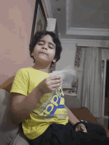 a young boy wearing a yellow adidas shirt holds a piece of paper