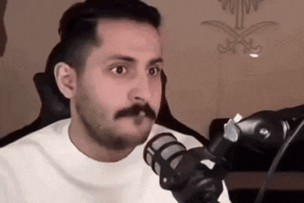 a man with a mustache is sitting in front of a microphone and talking into it .