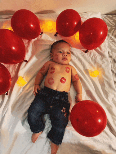a baby is laying on a bed with red balloons and kisses on his body