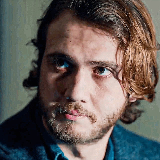 a close up of a man 's face with a beard and long hair