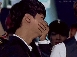 a man in a suit is covering his face with his hands while another man looks on