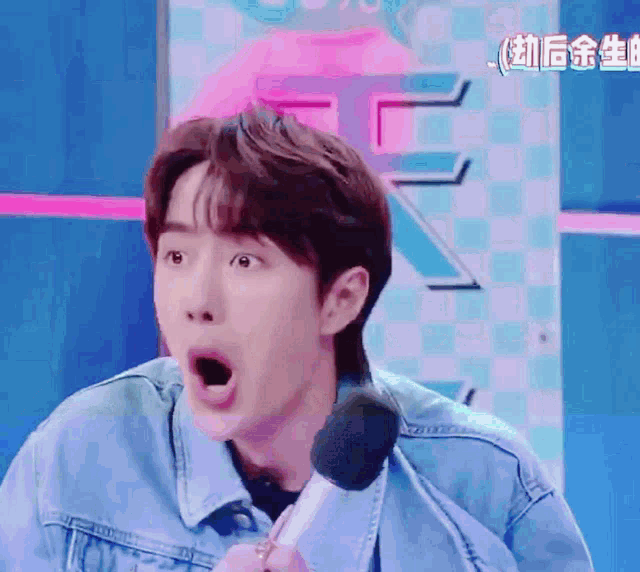 a man in a denim jacket is holding a microphone and making a funny face