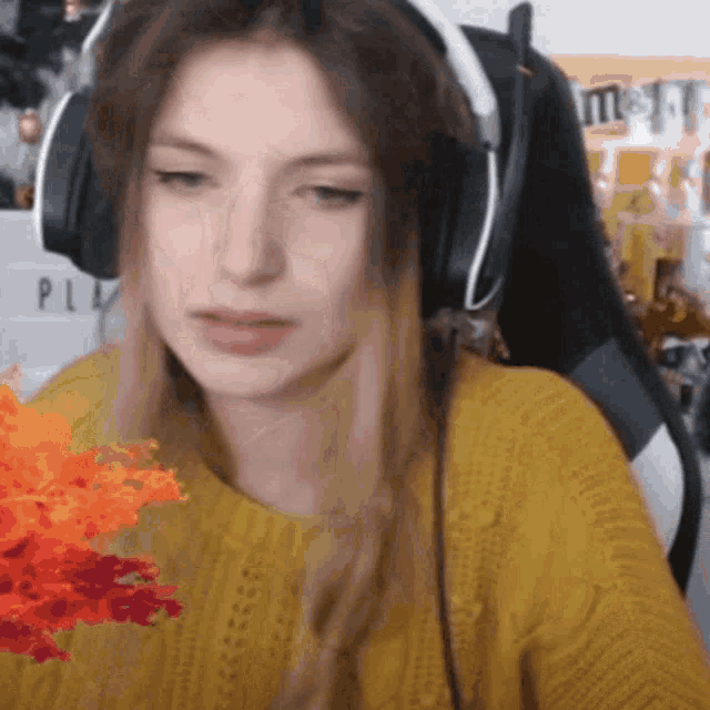 a woman wearing headphones and a yellow sweater looks at the camera