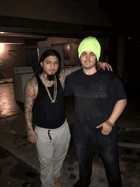 a man wearing a neon yellow hat is standing next to a man with tattoos