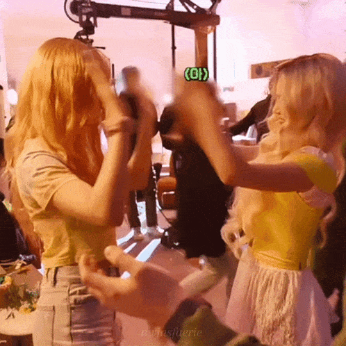 two blonde women are dancing in a room with a green sign that says oi