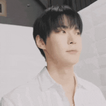 a young man wearing a white shirt and a necklace is looking at the camera .