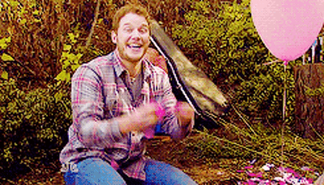 a man in a plaid shirt is sitting on the ground with balloons in the background