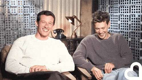 two men are sitting next to each other in chairs and smiling .